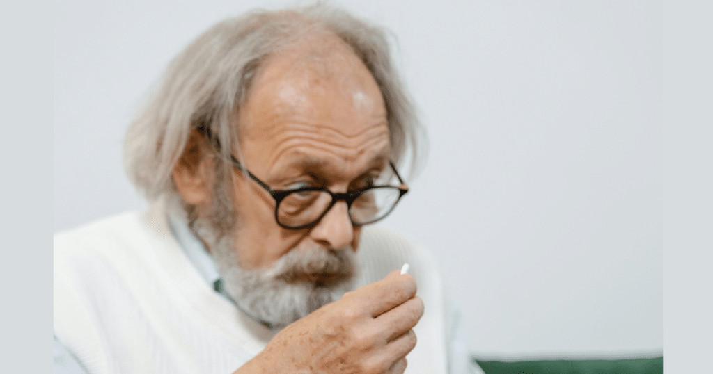 An elderly person looks uncertainly at a pill in their hand, not knowing what it is for.