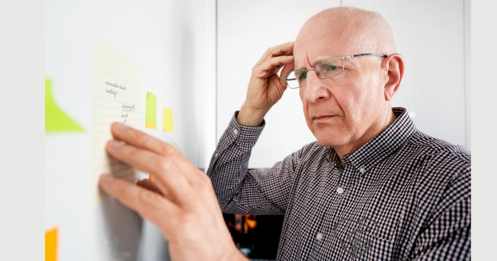 An elderly man holding his head with both hands, looking confused and overwhelmed, expressing memory loss and mental strain related to dementia.