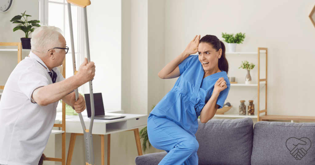 An elderly man at home threatening a young caregiver with his walking stick. The caregiver is stepping back while calmly trying to soothe the distressed loved one.