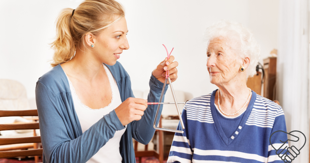 A young woman holding a vibrating tuning fork near the ear of an elderly woman with dementia in a home setting. The senior is listening intently, showing a moment of connection through sound.