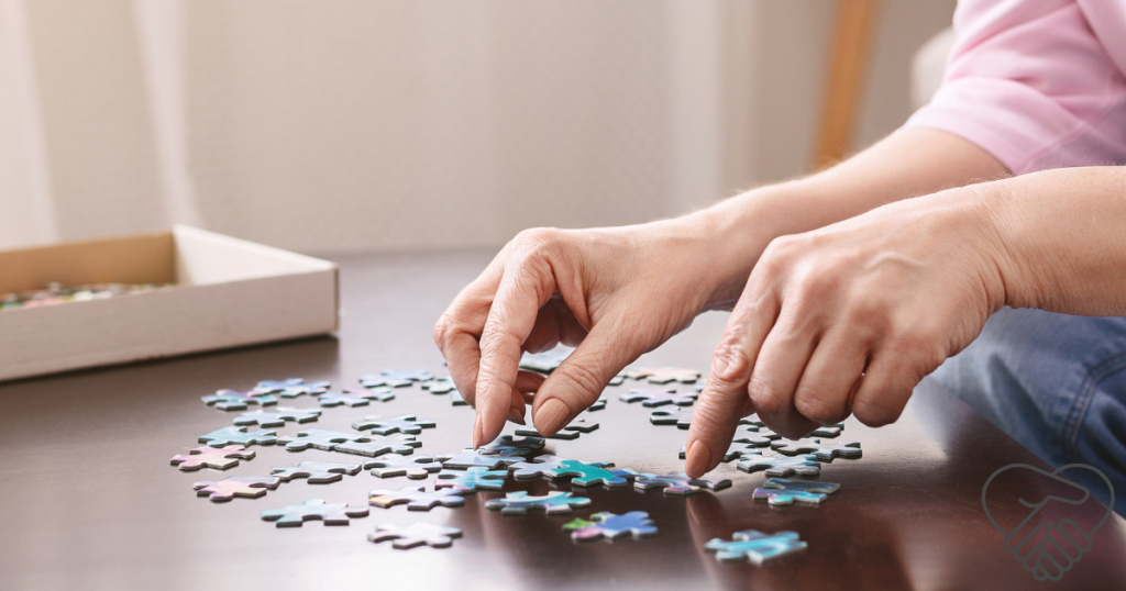 Közeli felvétel egy idősödő kézről, amint egy színes kirakós darabját illeszti a helyére a földön ülve. Otthoni környezet, fókuszban a mentális aktivitás.