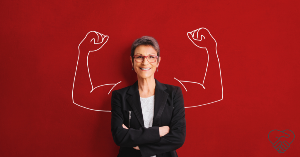 A smiling middle-aged woman standing against a red wall with her arms crossed, while a drawing of muscular arms behind her symbolizes her inner strength as a dementia caregiver.