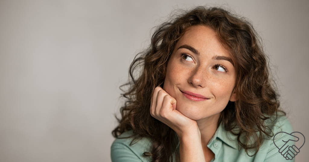 A thoughtful middle-aged woman smiling while resting her elbow on her hand. She is reflecting on changing her mindset, a key part of cognitive reframing for dementia caregivers managing stress at home.