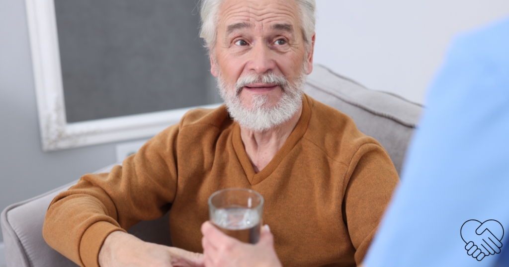 A person’s hand offering a glass of water to an elderly loved one with dementia who is politely refusing or hesitating.
