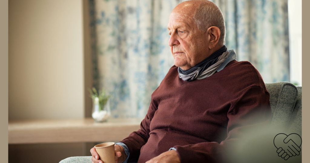 An elderly man sitting in an armchair at home, looking thoughtfully into the distance while holding a glass of water in his hands without drinking.