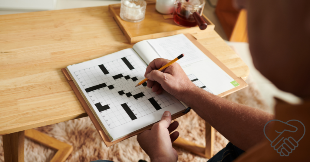 Close-up of a senior person's hands filling out a crossword puzzle with a pen at a desk.