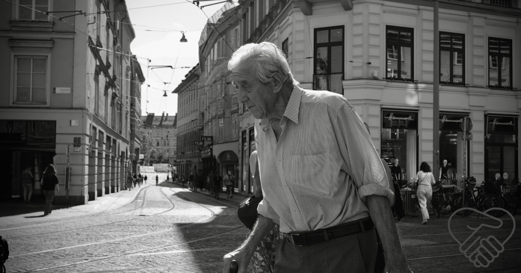 A black and white photograph of an older man walking hurriedly down the street with a confused, anxious expression, clutching a package in his hands, as if desperately searching for his way home
