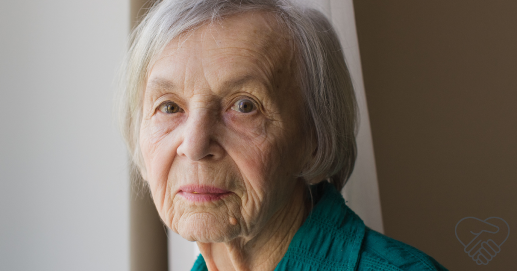 A close-up portrait of an elderly woman with gray hair looking directly into the camera with a confused, questioning expression, illustrating the uncertainty that comes with dementia.