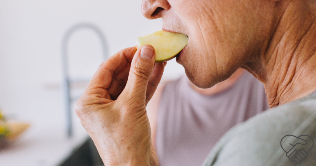 Close-up of an elderly woman at home bringing a small bite of fruit to her mouth.