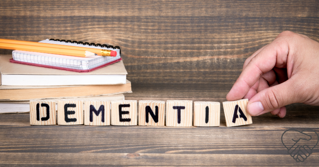 Understanding A hand is arranging wooden blocks with letters on a table to spell the word "dementia". The background is softly blurred.