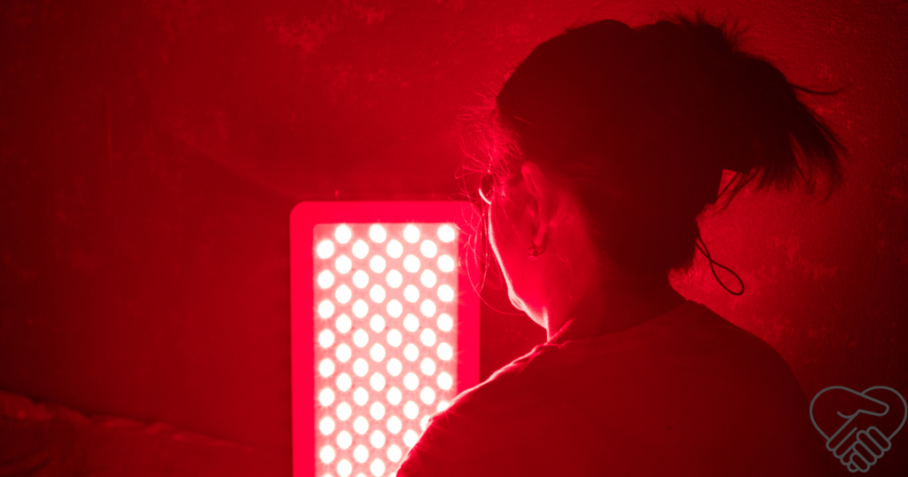 Dementia and Sleep Disorders: How Light Therapy Helps Achieve Quieter Nights Back view of a middle-aged woman sitting in front of a warm red light therapy lamp in a cozy home setting, preparing for a restful night.