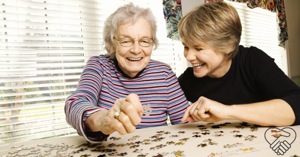 Can Cognitive Therapy Help Slow Memory Loss in Dementia? A young woman and an elderly woman with dementia laughing together while playing with a colorful jigsaw puzzle at home.